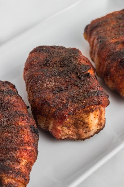 Baked pork chops wrapped in bacon on a platter.