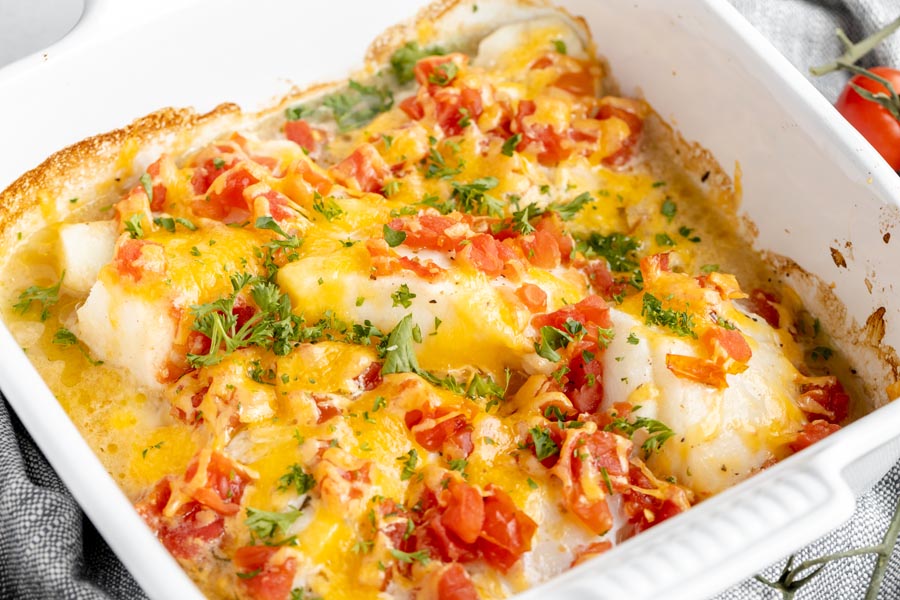 cheesy baked cod fish in a casserole dish topped with tomatoes