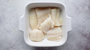 a white casserole dish with cod filets covering the bottom