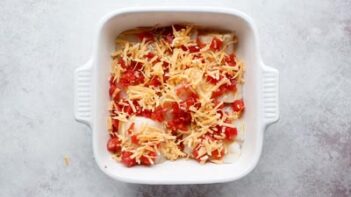 diced tomatoes and shredded cheddar cheese top raw cod fish in a casserole dish