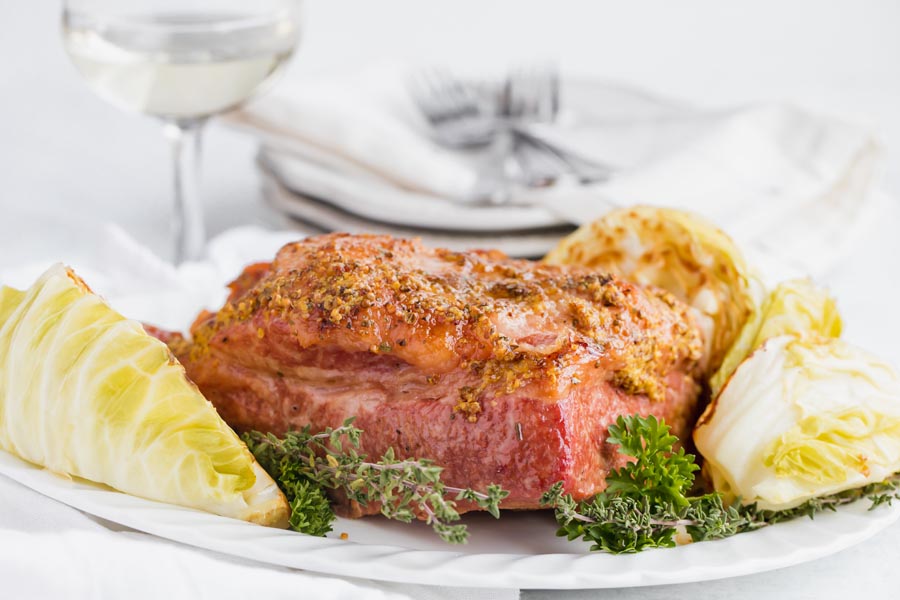 a dinner setting with white wine, plates and a platter of corned beef and cabbage