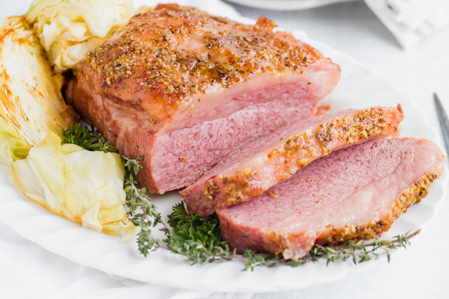 multiple cuts of baked corned beef on a platter next to sprigs of thyme