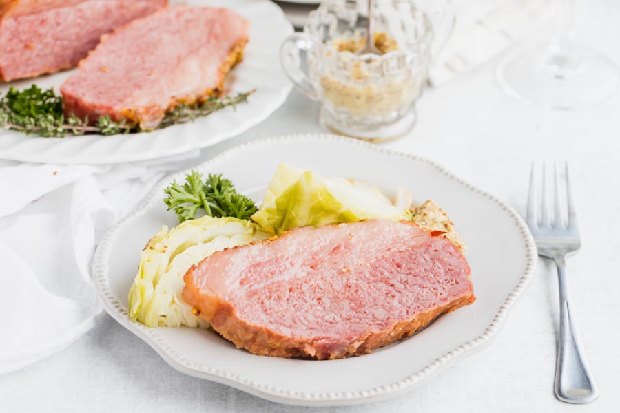 a thick slice of corned beef with cabbage and mustard on a plate next to a fork