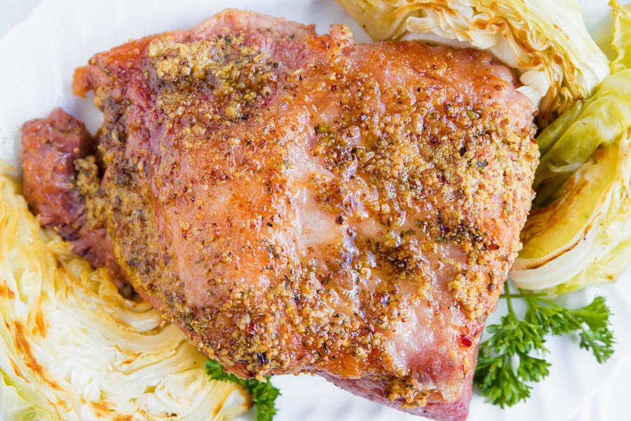 mustard and maple syrup crusted corned beef on a platter surrounded by cabbage and parsley