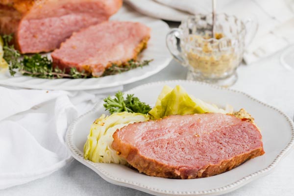 a slice of corned beef and cabbage on a dinner plate with mustard in a jar