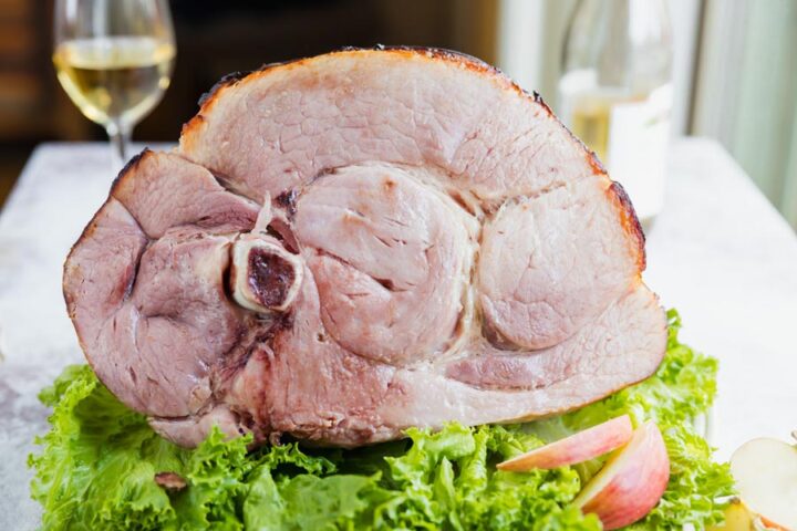 Roasted ham shank on a platter of greens with whole apple nearby.