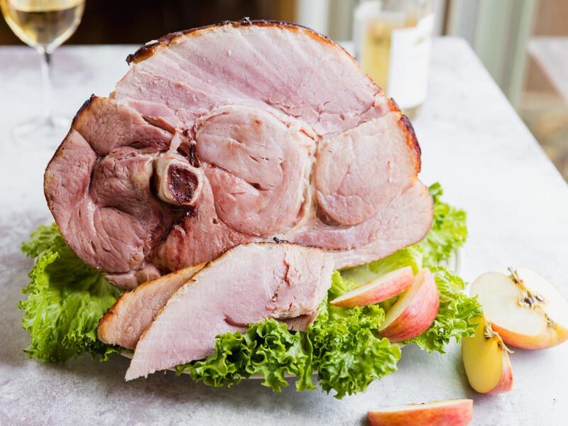 Sliced ham on a platter in front of a whole baked ham shank.
