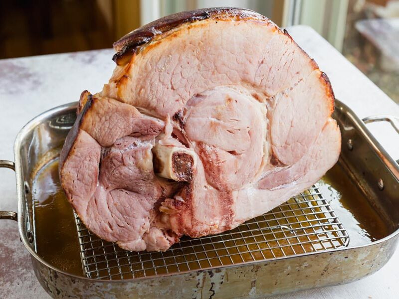 Baked ham shank sitting in a roasting pan on a rack.