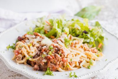 noodles and pasta sauce on a plate with parsley sprinkled and salad in the background