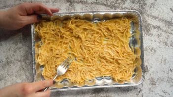 moving spaghetti pasta in a casserole dish with a fork