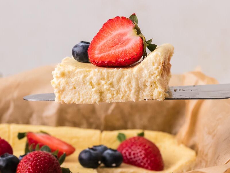 A thick slice of baked yogurt topped with a strawberry and blueberry being lifted from the baking dish.