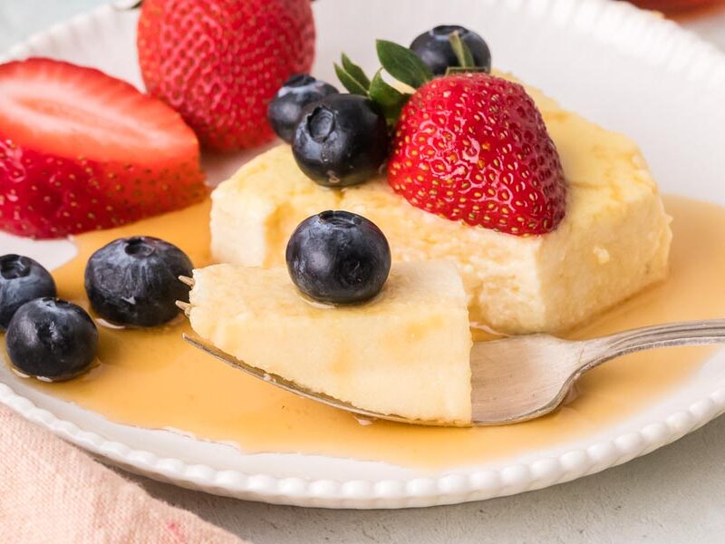 A fork holding a bite of creamy baked yogurt surrounded by fresh berries and maple syrup.