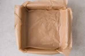 An 8-inch square baking pan lined with crumpled parchment paper for making baked yogurt.
