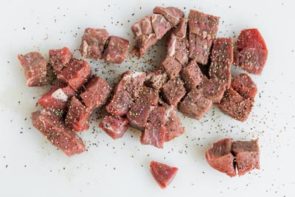 beef tips seasoning with salt and pepper on a cutting board