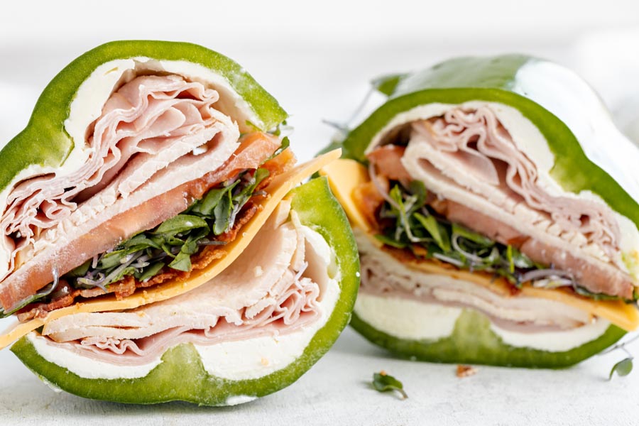 two sandwiches made from green bell peppers filled with turkey, ham, tomato and cheese