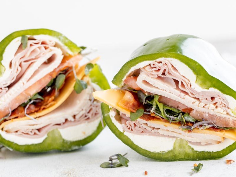 two bell pepper sandwiches filled with layers of deli meat, tomato, cheese and sprouts