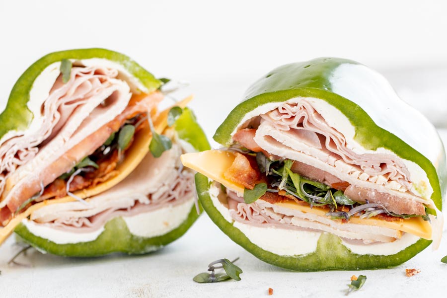 two bell pepper sandwiches filled with layers of deli meat, tomato, cheese and sprouts