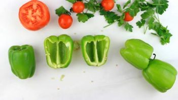 two bell peppers cut in half with three other green bell peppers around and a half a tomato