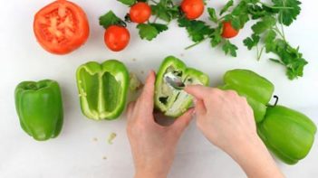 spreading a layer of cream cheese into the cavity of a half a bell pepper with bell peppers near by