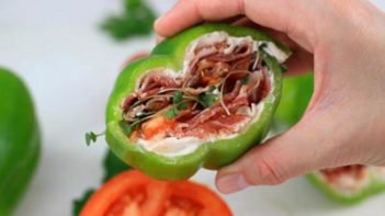 holding a half of a bell pepper sandwich filled with cold cuts and sprouts