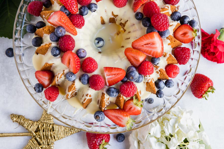 berry topped bundt cake with white chocolate on a cake plate with strawberries and blueberries