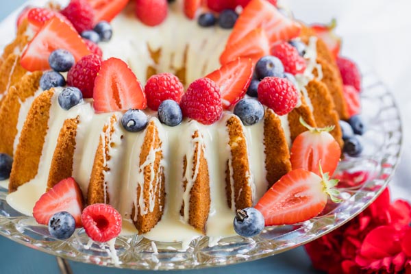 a colorful berry topped bundt cake on a clear cake stand