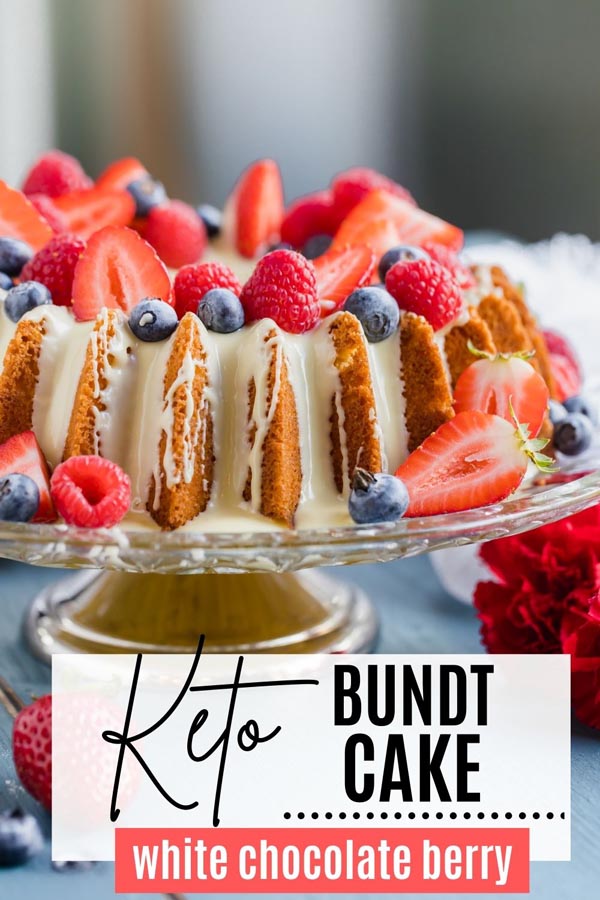 bundt cake dripping in white chocolate and topped with berries on a cake stand