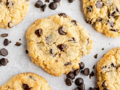 five golden brown chocolate chip cookies on the table with dark chips spread around