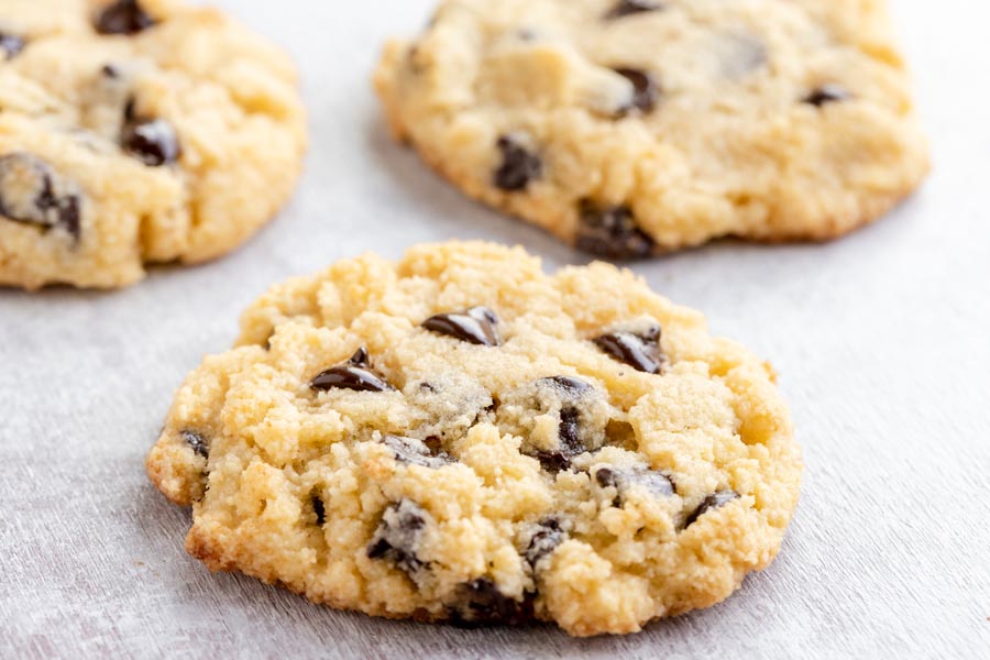 a plump freshly baked chocolate chip cookie on a table with two other cookies in the background