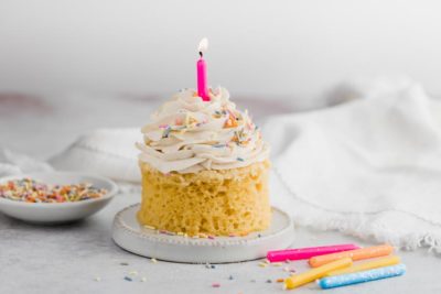 a lit candle on a small birthday cake with sprinkles and candles scattered near
