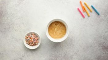 cake batter in a white ramekin next to sprinkles and candles