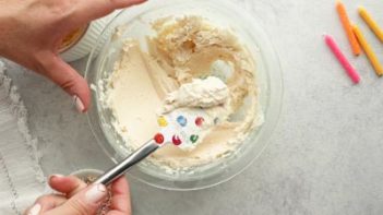 a spatula with creamy white frosting over a bowl of frosting with candles near