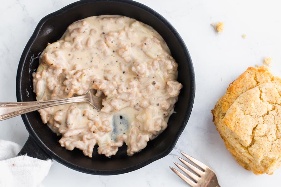 cast iron skillet with sausage gravy and side of keto biscuits