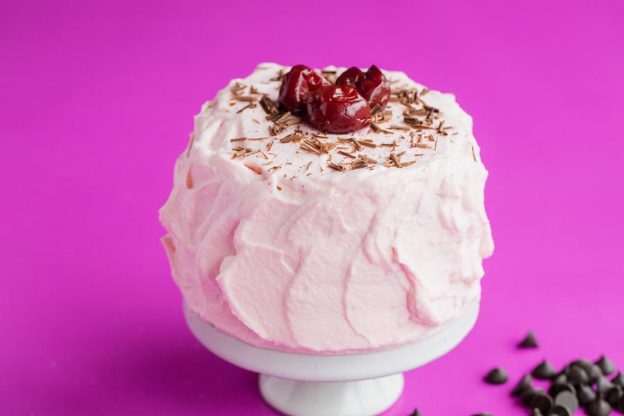 a mini pink cake on a bright pink background topped with cherries