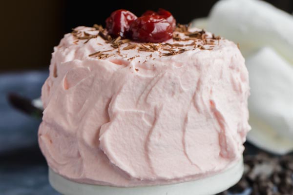 a frosted cake topped with crushed cherries and chocolate