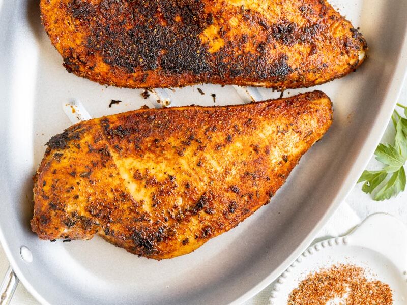 Blackened chicken breasts in a skillet with a small dish of seasoning.