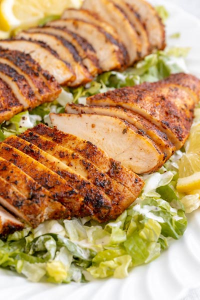 Sliced charred chicken breast over a bed of chopped romaine lettuce.