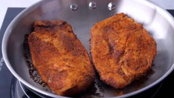 Blackened chicken searing in a stainless steel skillet.