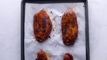 Blackened chicken baked on a parchment lined baking tray.