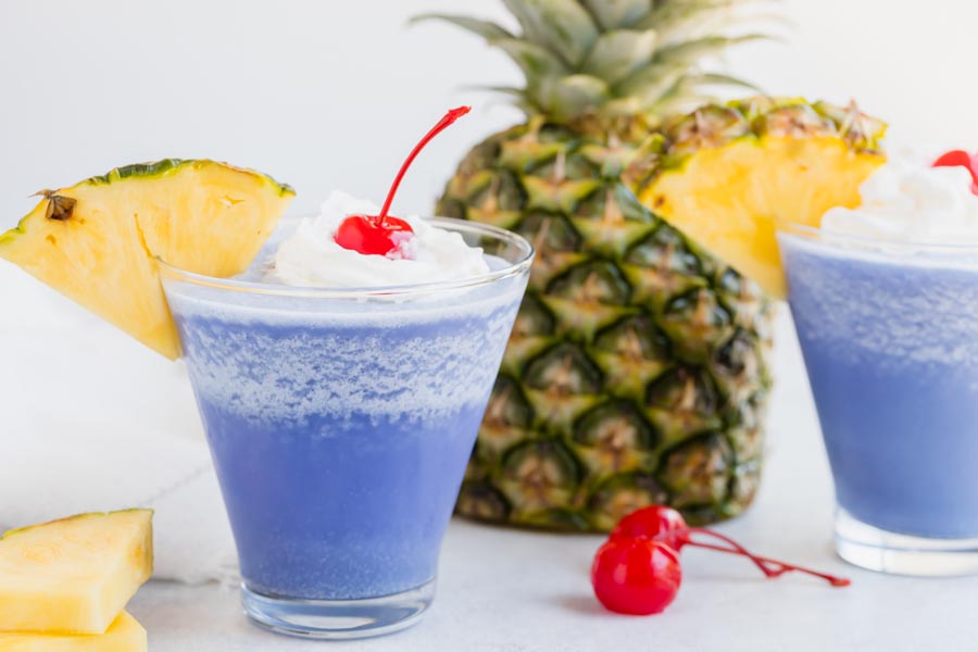 a frosty blue cocktail with a pineapple slice a cherries around it