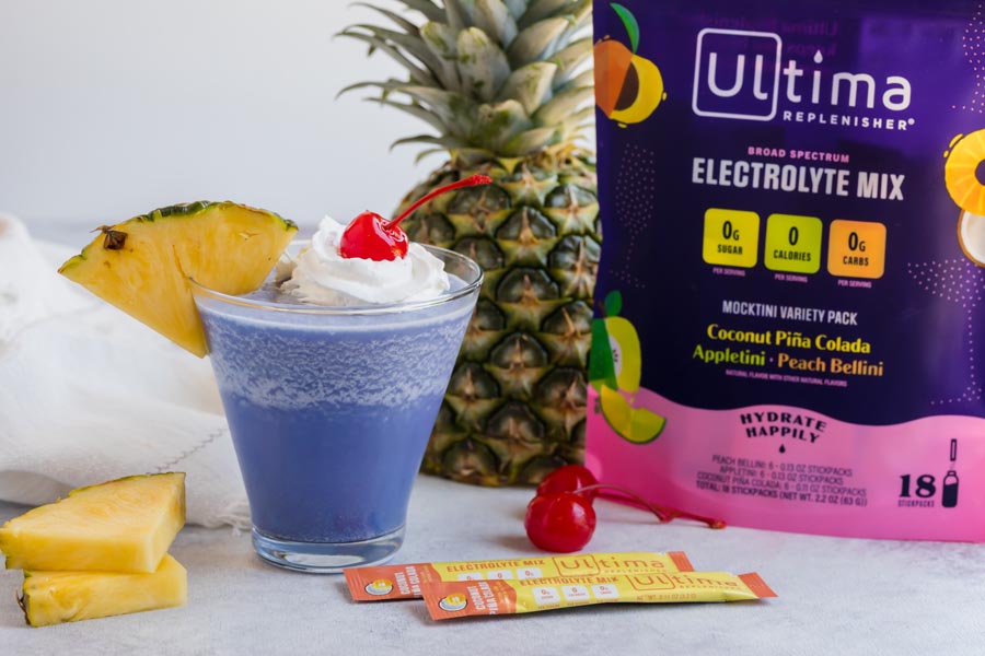 a bag of ultima mocktini mixes sits next to a pineapple and a blue pina colada drink
