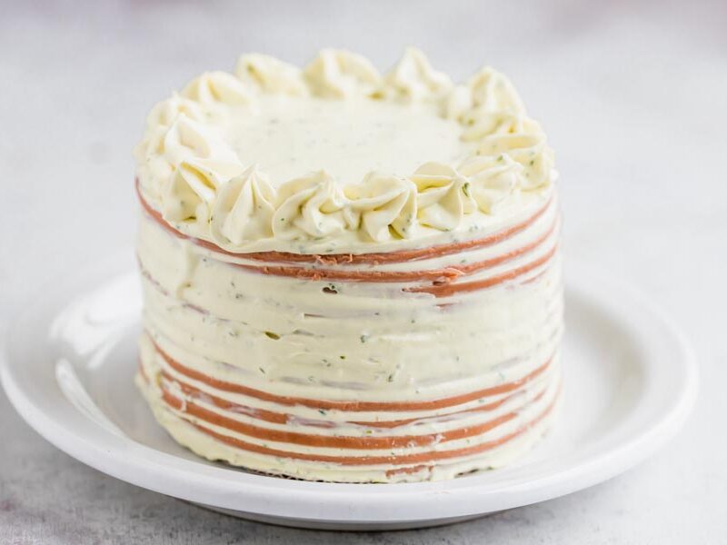 A small cake made out of sliced bologna and a creamy cheese frosting with stars piped on top.