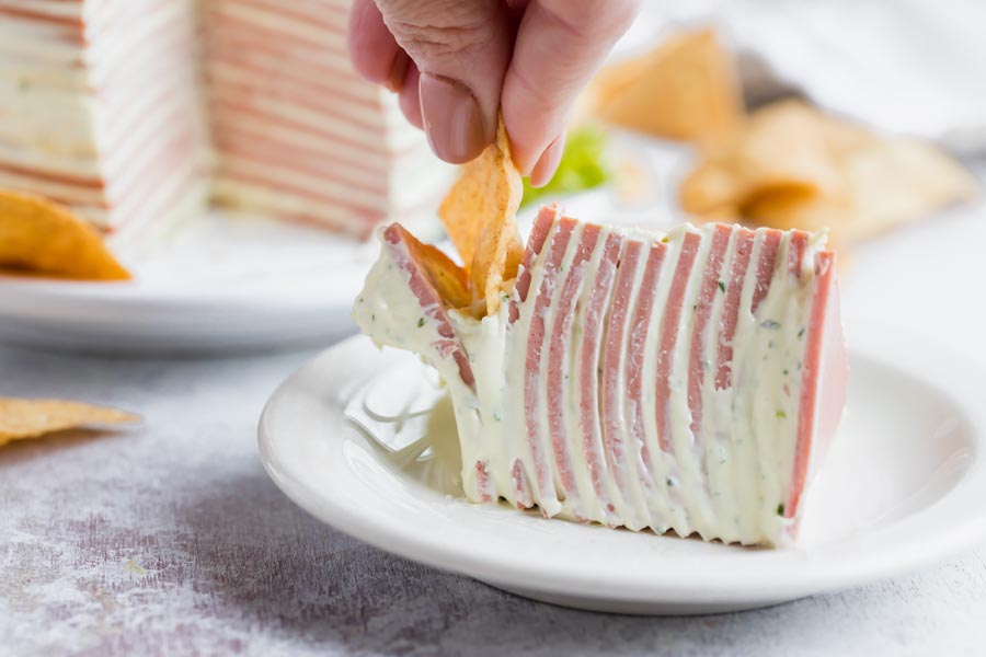 A hand dipping a chip into a slice of bologna cake.
