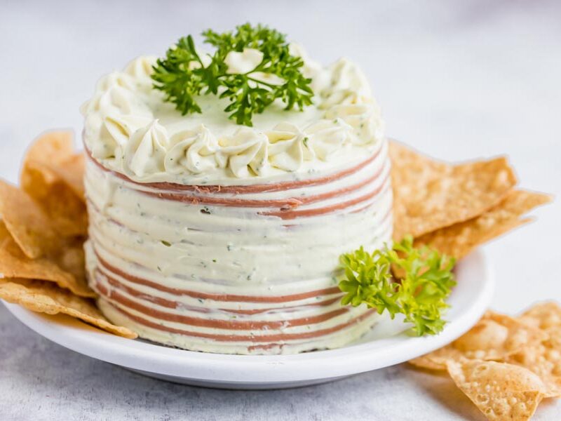 A small bologna cake on a plate with chips around and topped with parsley.