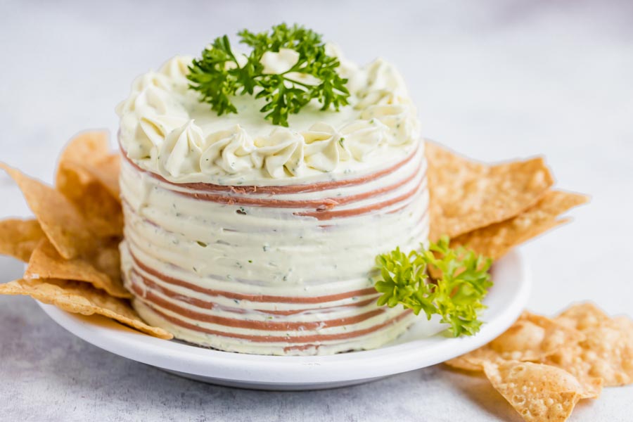 A small bologna cake on a plate with chips around and topped with parsley.