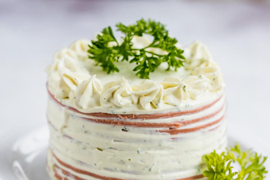 A multi-tiered meat cake topped with a herb cheese filling and frosting.