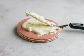 A cake spatula spreading on cream cheese on top of a slice of bologna.