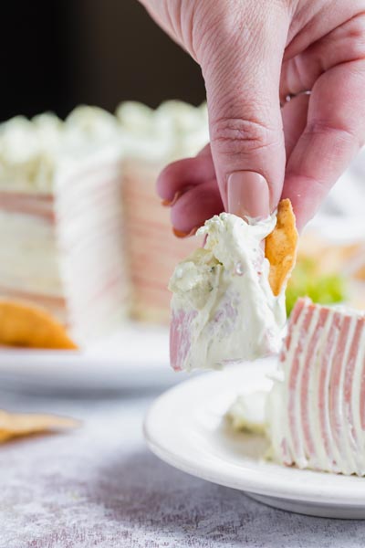 A hand holding a chip with a slice of bologna and cream cheese on it.