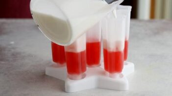 pouring a milky liquid in a popsicle mold over a red frozen layer