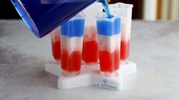pouring blue liquid into a popsicle mold over a white and red layer